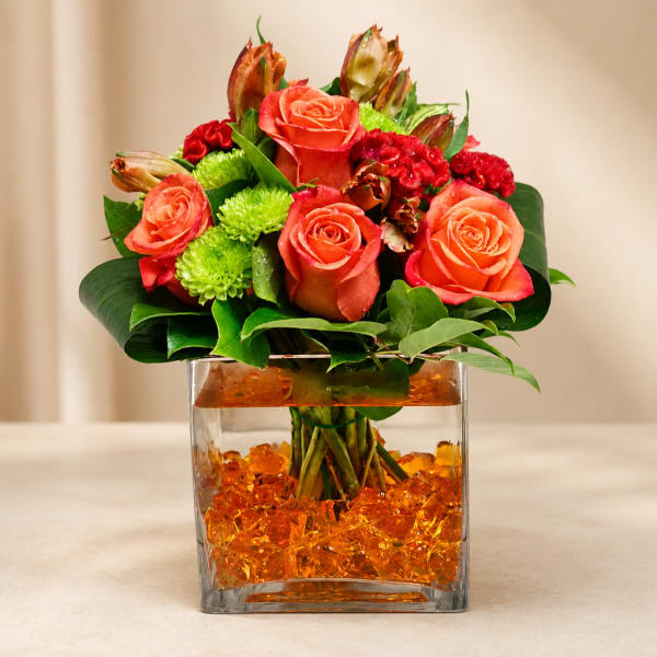 Orange roses and red flowers arranged in a square glass vase