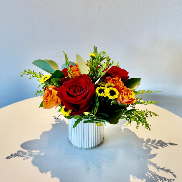 Red and orange roses in a ribbed white vase with small yellow flowers