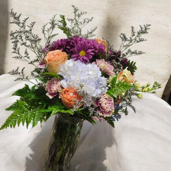 Mixed bouquet of purple, peach, and white flowers in a glass vase