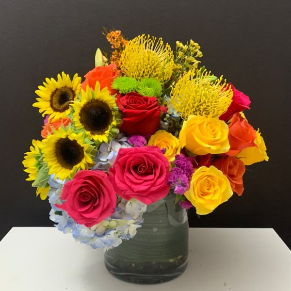 Colorful bouquet of roses, sunflowers, and hydrangeas in a glass vase