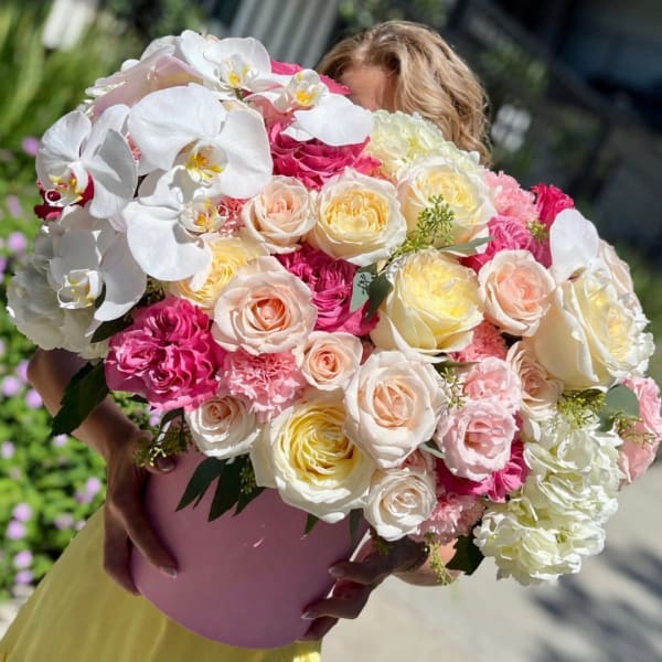Large bouquet of white orchids, pink roses, and pale blooms in a pink hatbox