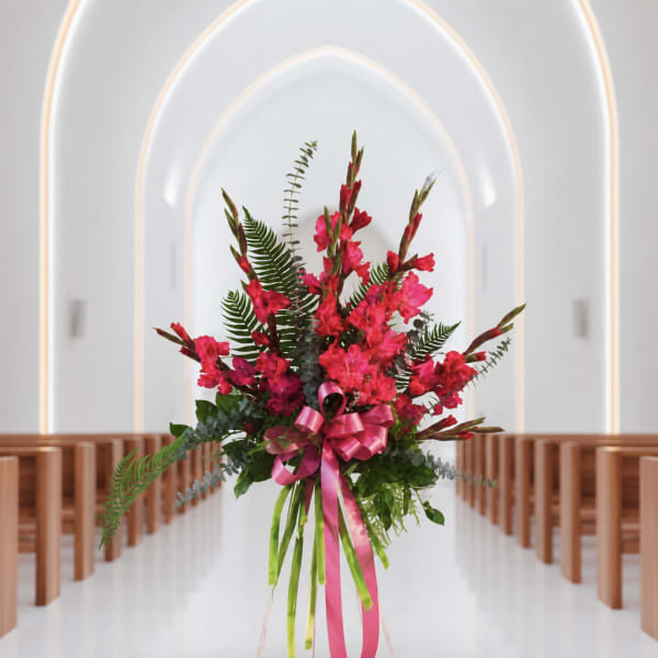 Tall pink floral arrangement with a ribbon in a church aisle