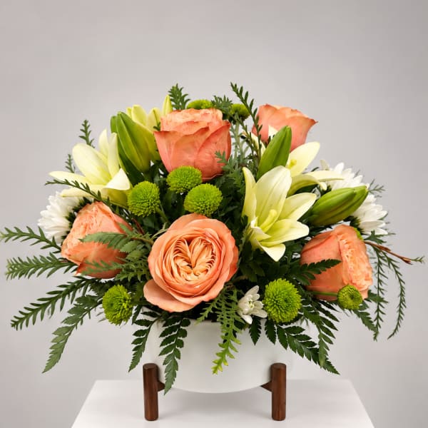 Peach roses and white lilies arranged in a white vase