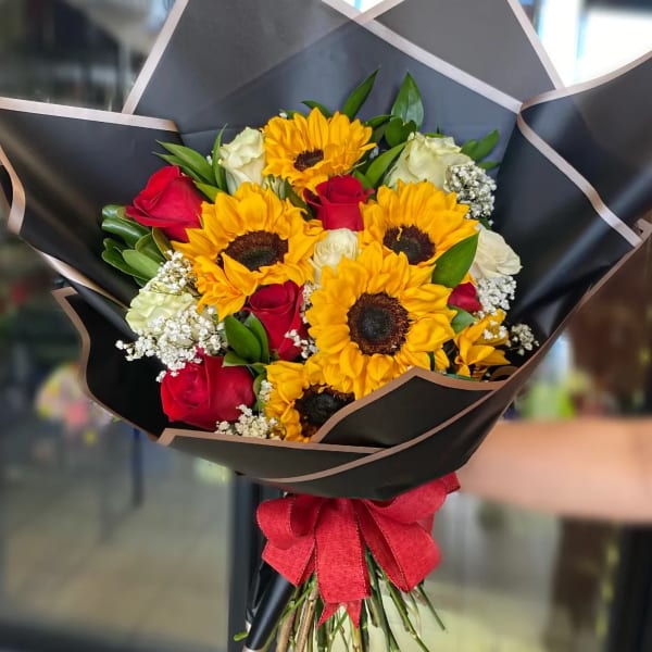 Bouquet of sunflowers and red roses wrapped in black paper with a red bow