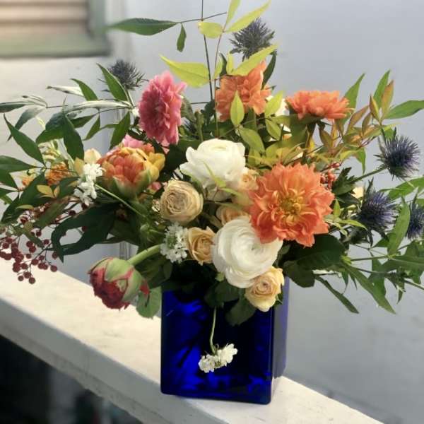 Asymmetrical bouquet of orange dahlias and cream roses in a cobalt blue glass cube vase