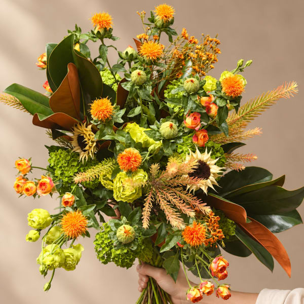Handheld bouquet with orange blooms and green flowers in a loose, airy design