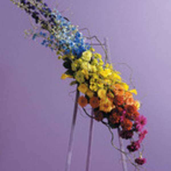 Tall multicolored floral arrangement on a stand against a purple background