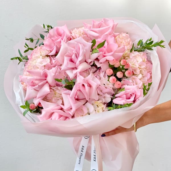 Pink rose bouquet with pale hydrangeas and berry accents wrapped in blush paper