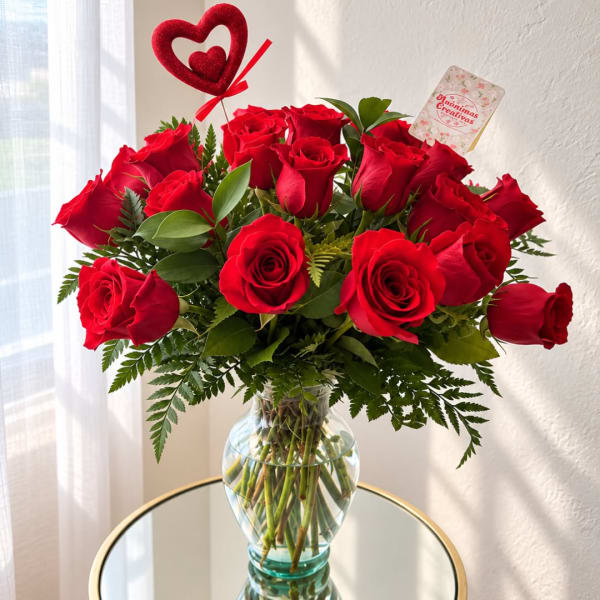 Red roses arranged in a clear glass vase with a heart topper