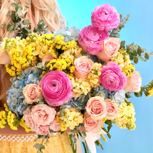 Large bouquet of pink, yellow, and blue flowers held in front of a person