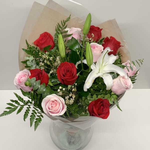 Bouquet of red and pink roses with a white lily in a glass vase