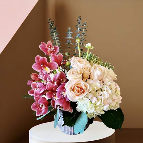 Pink orchids and pale roses arranged in a woven basket