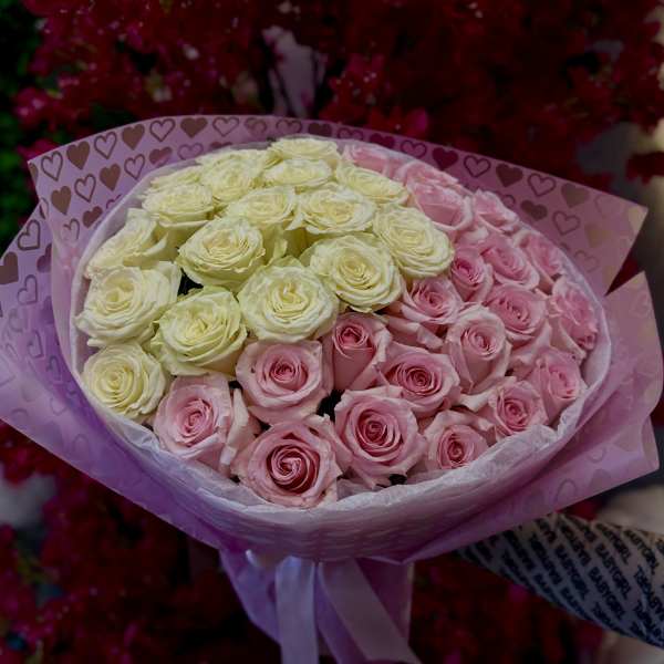 Bouquet of pink and cream roses wrapped in heart-patterned paper