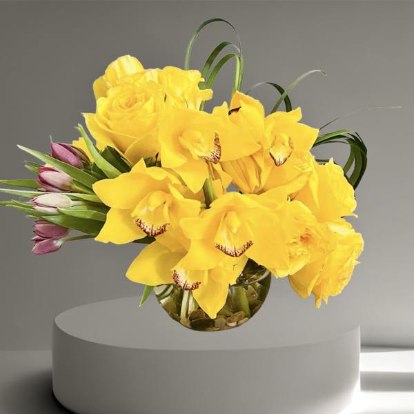 Yellow roses and orchids in a round glass vase