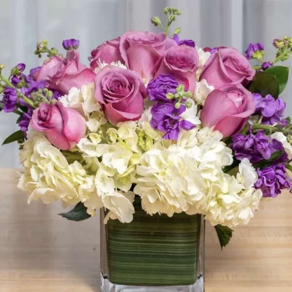 Pink roses and white hydrangeas in a square glass vase with purple accents