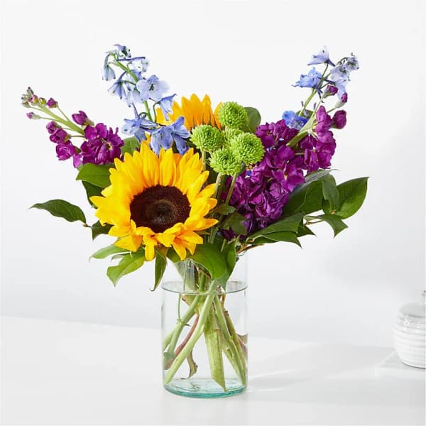 Sunflowers and purple-blue flowers in a clear glass vase