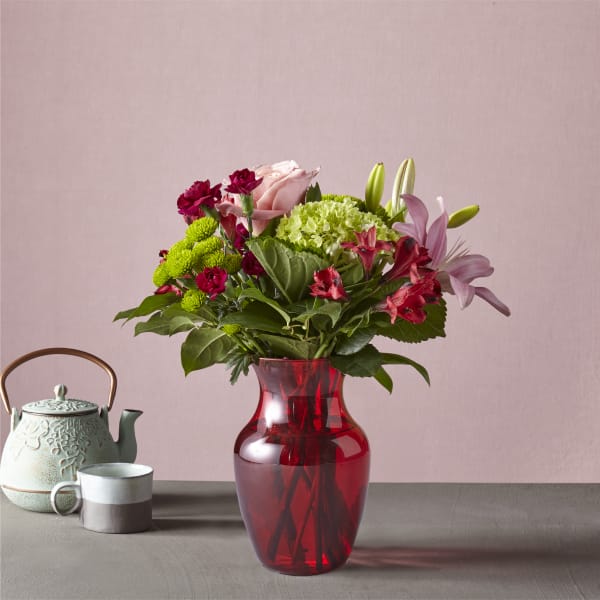 Mixed bouquet in a red glass vase with a teapot and mug beside it