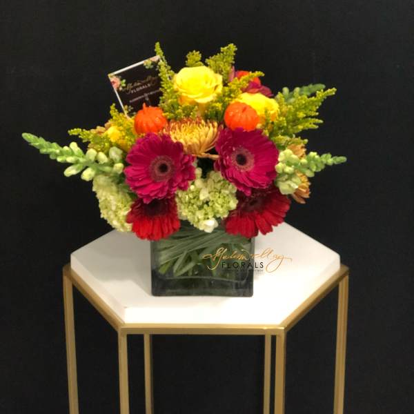 Bright mixed bouquet in a square glass vase with yellow, pink, and red blooms