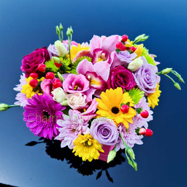 Colorful mixed bouquet with roses, orchids, and daisies in a pink container