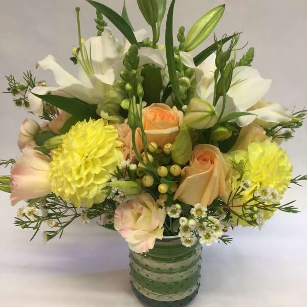Mixed bouquet of white and peach flowers in a green glass vase