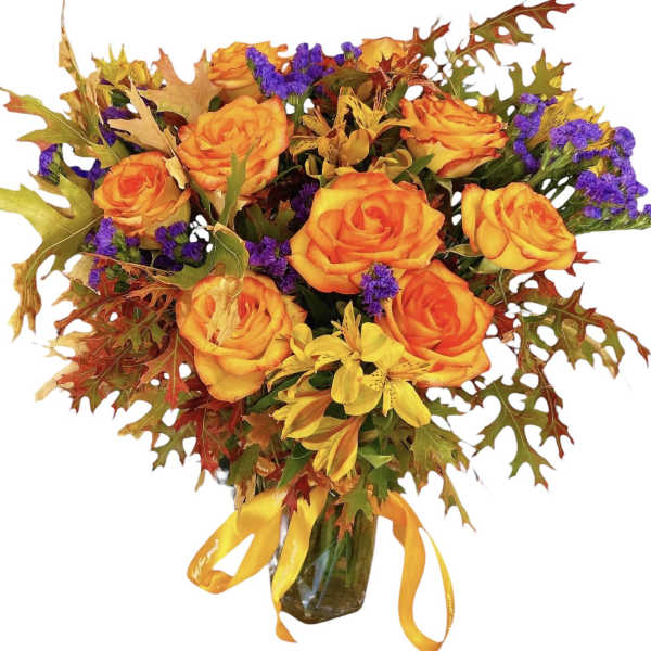Orange roses in a glass vase with autumn leaves and purple filler flowers
