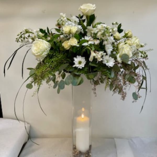 White floral arrangement in a tall clear vase with a candle inside