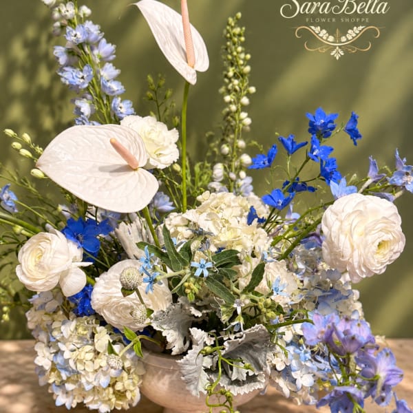 Large floral arrangement with white anthuriums, ranunculus, and blue blooms in a vase