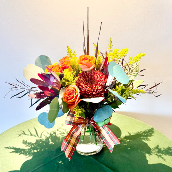 Orange roses and a red chrysanthemum in a glass vase with a plaid ribbon