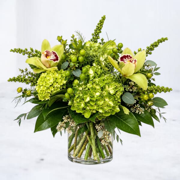 Green floral arrangement with orchids and hydrangeas in a glass vase