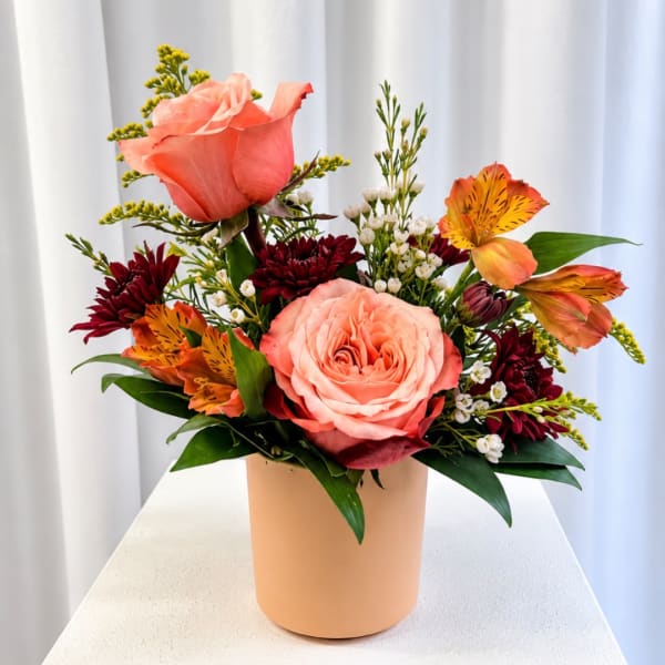 Peach roses and orange alstroemeria in a tan vase