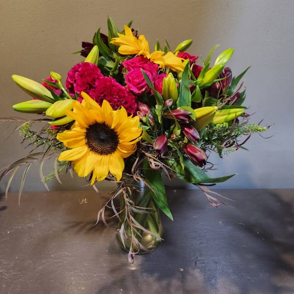 Bright mixed bouquet with sunflowers, pink roses, lilies, and a gold vase