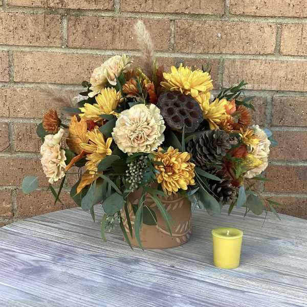 Autumn flower arrangement in a decorative pot with a small yellow candle nearby
