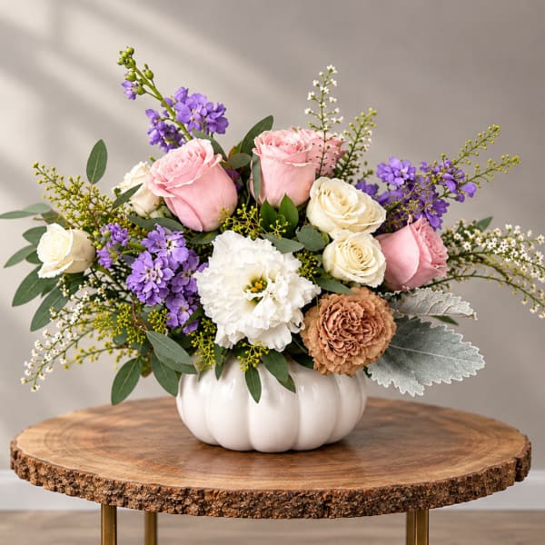 Pink and white roses with purple flowers in a white pumpkin vase