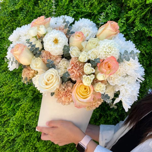 Handheld bouquet of cream, peach, and white flowers in a white wrap