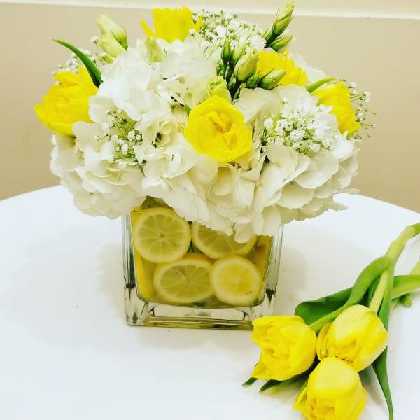 Yellow and white flower arrangement in a square glass vase with lemon slices