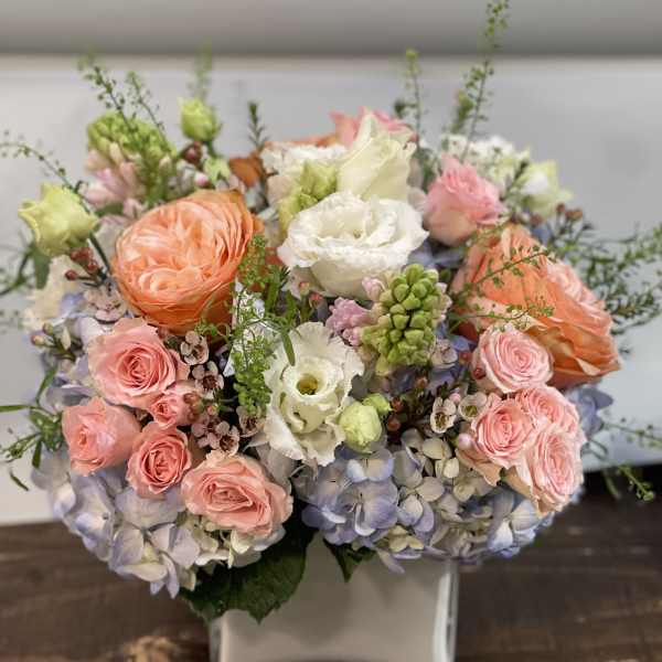 Pastel bouquet of roses, hydrangeas, and white blooms in a square vase