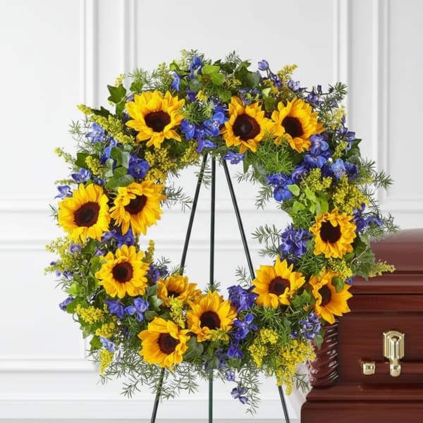 Sunflower and blue floral wreath on a stand beside a casket