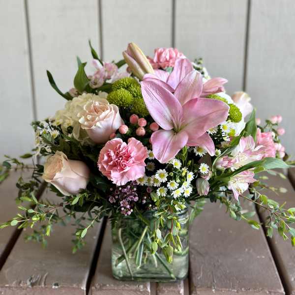 Pink lilies and roses arranged in a square glass vase