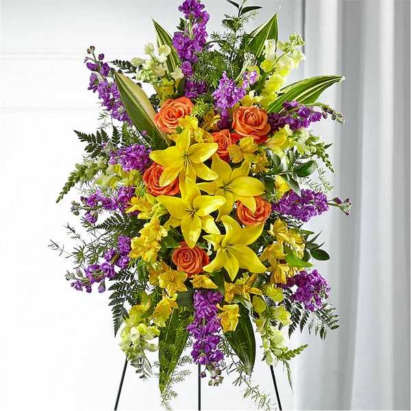 Tall floral standing spray with yellow lilies, orange roses, and purple flowers