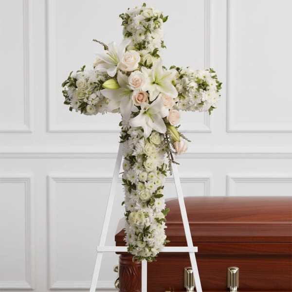 White floral cross on an easel beside a casket