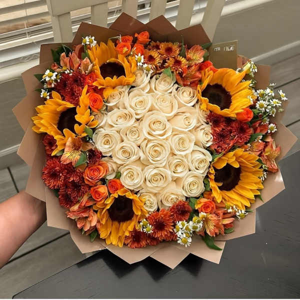Bouquet of cream roses with sunflowers and orange blooms in brown paper