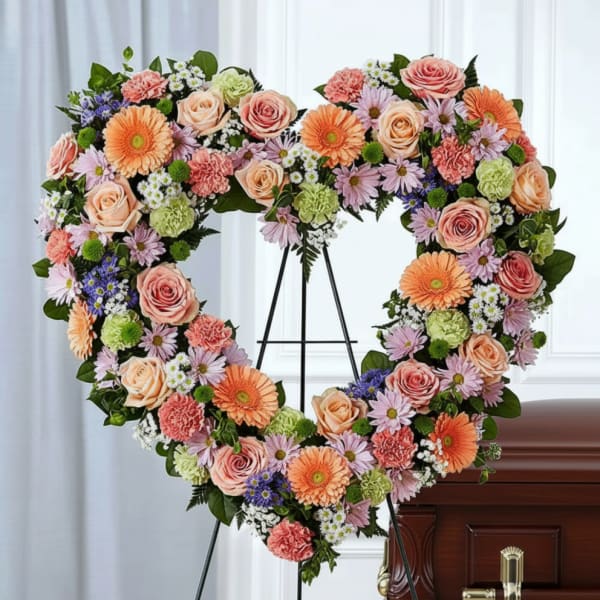Heart-shaped floral spray on an easel beside a casket