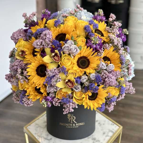 Bouquet of sunflowers, yellow roses, and purple flowers in a black hat box