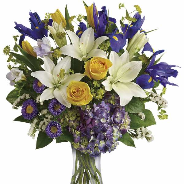 Bouquet of white lilies, yellow roses, purple irises, and hydrangea in a glass vase