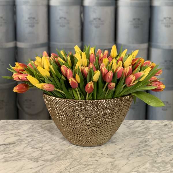 Yellow and pink tulips arranged in a gold textured vase