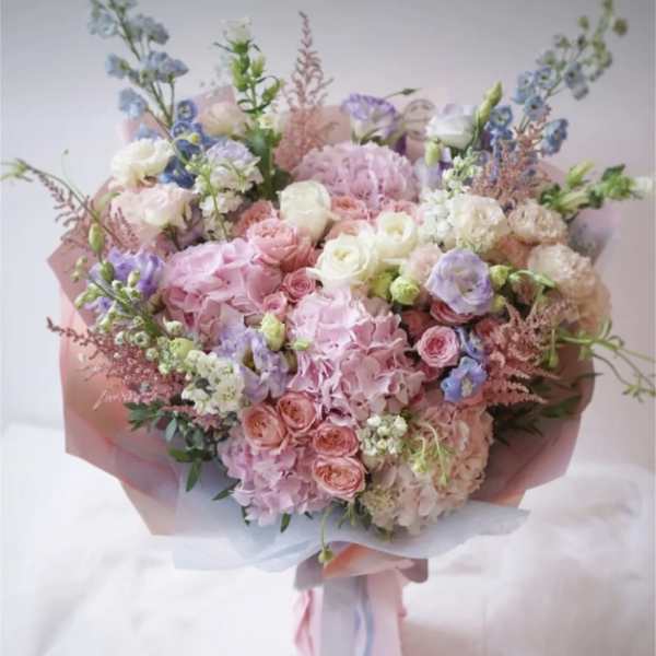 Large pastel bouquet of pink, white, and blue flowers wrapped in pink paper