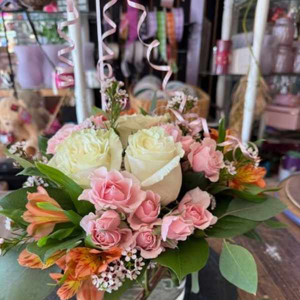Pink and white rose bouquet in a glass vase with orange flowers