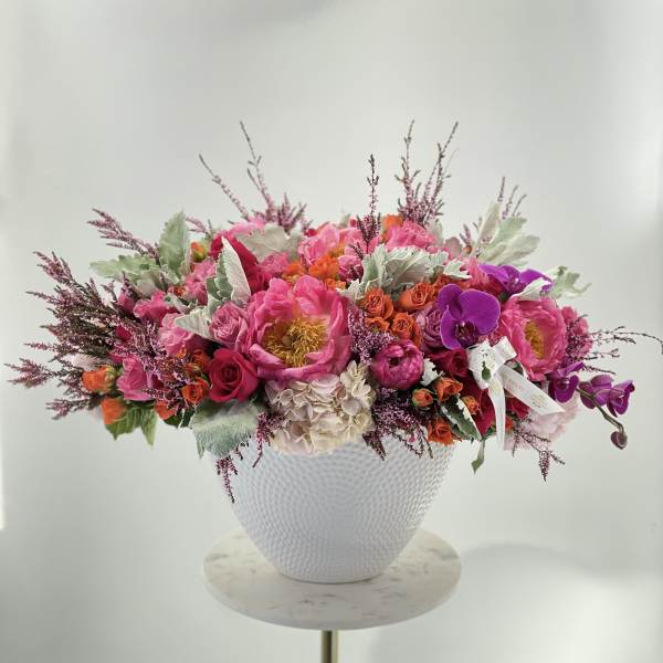 Bright pink and purple floral arrangement in a white textured vase