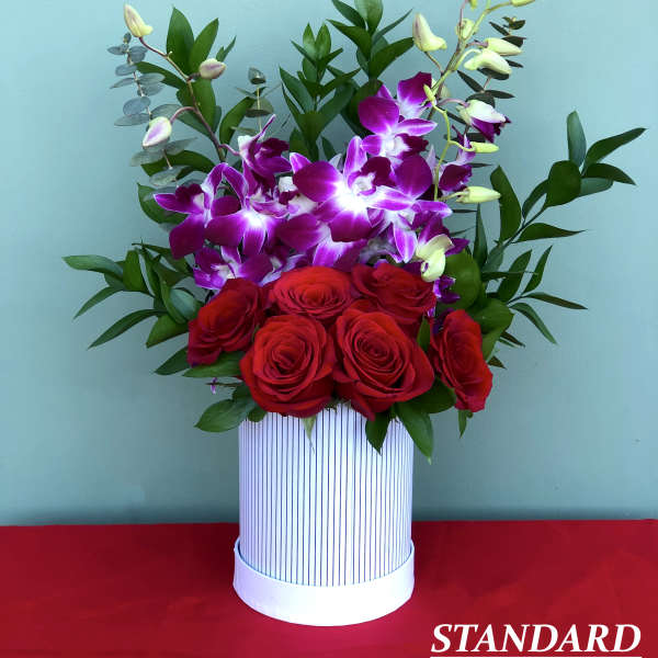 Red roses and purple orchids in a striped white box