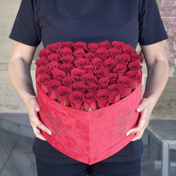 Heart-shaped box filled with red roses being held by a person